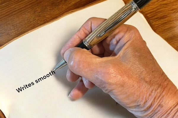 Picture showing a hand using a hand turned Gatsby pen on a white piece of paper on a desk. 