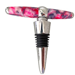 A handmade bottle stopper featuring a silver base and a black rubber stopper. The handle, crafted horizontally from a shiny material in vibrant pink  with purple swirls.  Hand turned by Paul’s Hand Turned Creations for the collection wine toppers. 