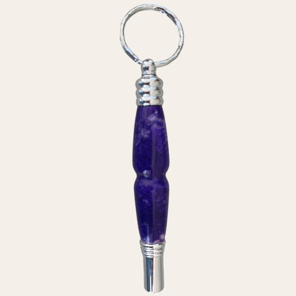 A unique gift from Paul's Hand Turned Creations, the Purple Passion #1 Secret Compartment Key Chain with Safety Whistle features a metal whistle with a handle made of textured purple material. The ergonomic, curvy design ensures comfort. The back is primarily all purple coloring. 