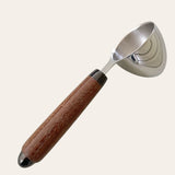 Hand-turned coffee scoop by Paul's Creations with Brazilian cherry wood handle on plain background.