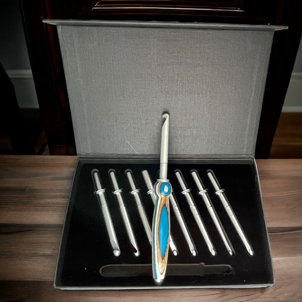 A crochet hook set with eight metal hooks of varying sizes is displayed in a gray case. One hook, featuring a blue and wood-patterned handle, is prominently placed in the center, while the other seven hooks are lined up in slots, arranged neatly behind it.