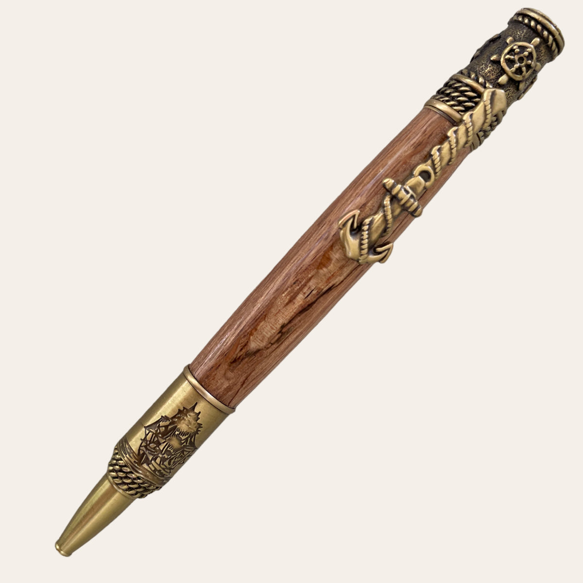 Paul's Hand Turned Creations presents the Hand Turned Nautical Pen With Antique Brass Trim-Laurel Oak, featuring a barrel made from spalted oak and detailed with intricate metal accents, including an anchor and rope design near the top and a nautical star with additional rope details near the tip. This pen exudes a vintage, maritime-inspired aesthetic.