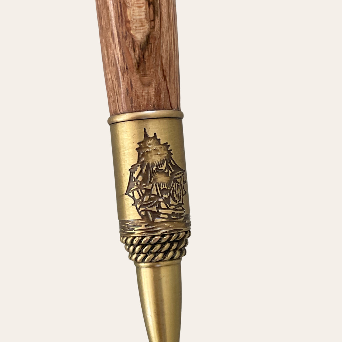 A detailed image of the Hand Turned Nautical Pen With Antique Brass Trim-Laurel Oak by Paul's Hand Turned Creations. The wood, made of spalted laurel oak, is textured and smooth. The antique brass section features an intricately engraved design of a ship sailing with full sails and a decorative rope pattern near the transition point, emphasizing its nautical theme.