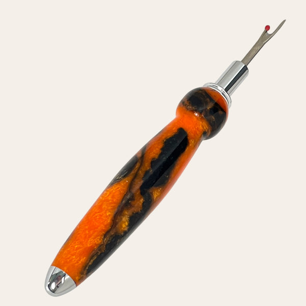 A close-up of the Hand Turned Resin Single Blade Seam Ripper - Sunset Blaze from Paul's Hand Turned Creations reveals its intricate design, featuring a sharp stainless steel blade perfect for precision work.