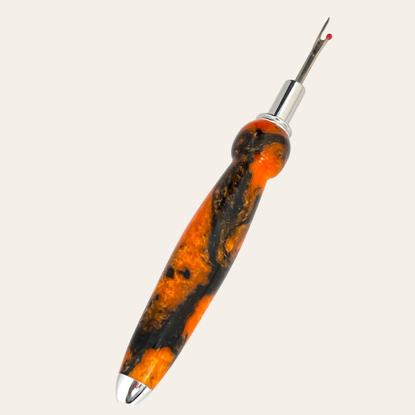 Introducing the Hand Turned Resin Single Blade Seam Ripper - Sunset Blaze by Paul's Hand Turned Creations, an essential sewing tool featuring a sharp stainless steel blade with a small red ball at the end and a striking orange and black marbled handle. Perfect for cutting and removing stitches in fabric.