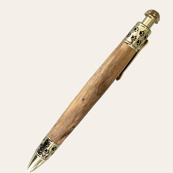 The Spalted Tamarind Dog Click Pen With Gold Trim by Paul's Hand Turned Creations features ornate brass accents on the cap, clip, and tip, showcasing intricate designs. The pen has a polished finish, combining a rustic wooden body with elegant metallic details. This personalized accessory is perfect for any dog lover looking to add charm to their writing tools.