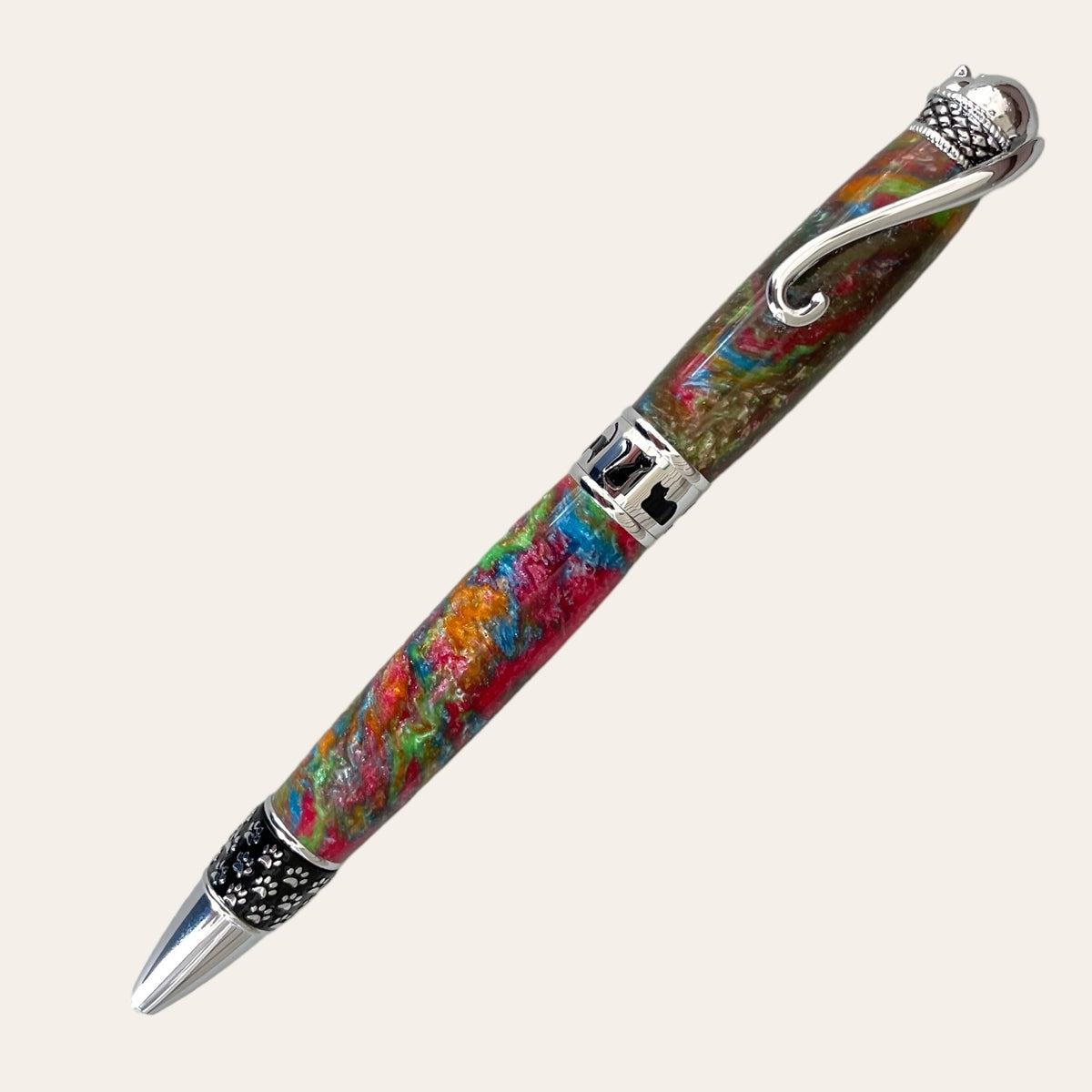 Introducing the Hand Turned Cat Pen on Chrome Trim- Calico by Paul's Hand Turned Creations: a vibrant twist pen that evokes the charm of a calico cat with its multicolored resin body featuring beautiful swirls of red, green, blue, and yellow. It is elegantly complemented by silver accents, including a decorative clip shaped like a dragon and intricate band designs. The black tip enhanced with silver details completes this meticulously crafted writing instrument.