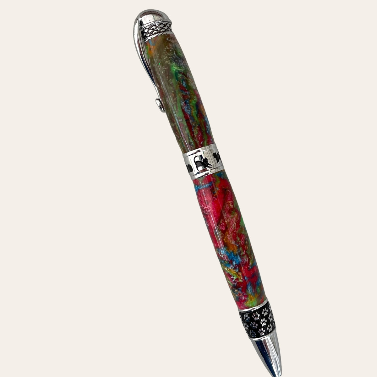 Introducing the Hand Turned Cat Pen on Chrome Trim- Calico by Paul's Hand Turned Creations. This vibrant, handcrafted pen features a captivating blend of green, red, and brown swirls. It has silver-tone decorative elements including an intricate cap and a band adorned with a silhouetted figure. The clip and tip are also silver-toned, with the grip area showcasing a unique star pattern.