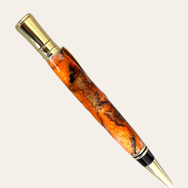 Introducing the Executive Pen With Gold Trim- Tangerine from Paul's Hand Turned Creations. This exquisite pen boasts intricate orange and black swirls in the barrel, providing a smooth writing experience. It features sophisticated gold-colored accents on the clip, tip, and top. The pen seamlessly blends rustic charm with elegant design elements, showcasing handcrafted excellence.