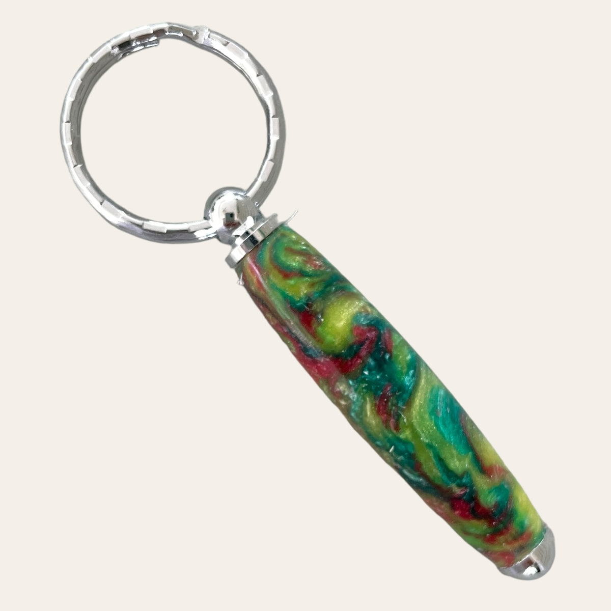 The Small Resin Keychain - Mysterious by Paul's Hand Turned Creations features a colorful, cylindrical pendant with a marbled pattern in red, green, blue, and yellow tones. This unique pendant is attached to a silver circular key ring.