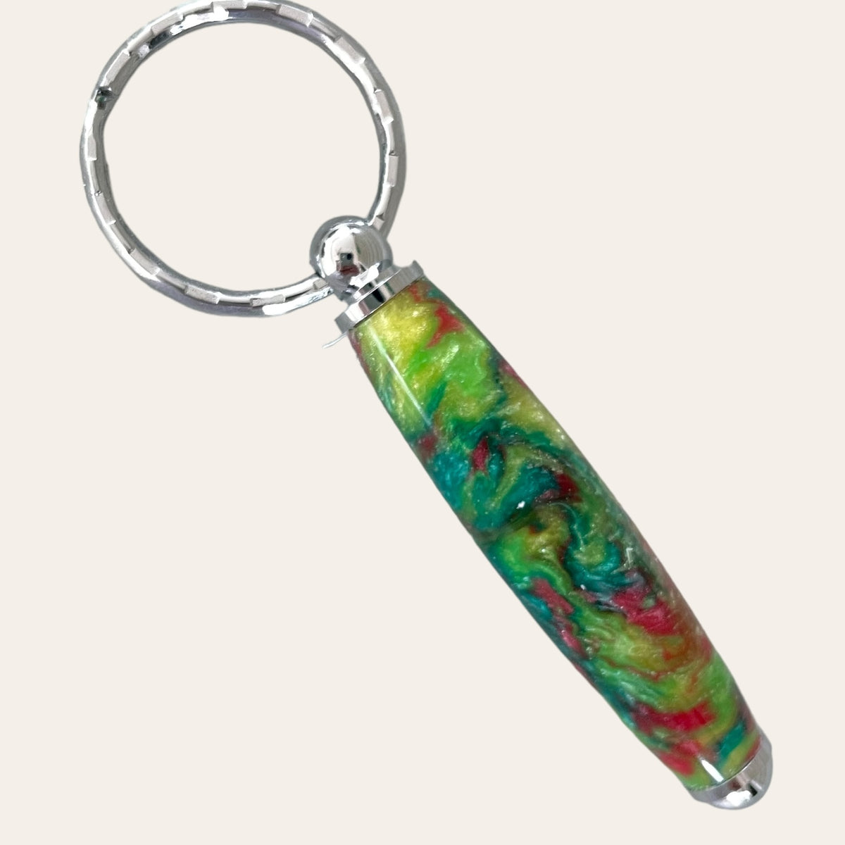 The Small Resin Keychain - Mysterious by Paul's Hand Turned Creations is a handcrafted piece featuring a metal ring and a colorful resin handle. The handle showcases an abstract swirl pattern in vibrant shades of green, yellow, red, and blue. The polished metal components offer a stunning contrast to the vivid colors of the resin, making it a unique and eye-catching accessory.