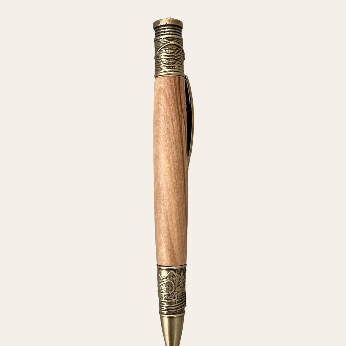 A Fly Fishing Pen from Paul's Hand Turned Creations, crafted from Exotic Bethlehem Olive Wood and adorned with antique brass trim. The metal sections feature intricate fly fishing patterns, and the pen includes a sturdy clip. Its smooth, polished wood finish beautifully contrasts with the antique metal design elements.