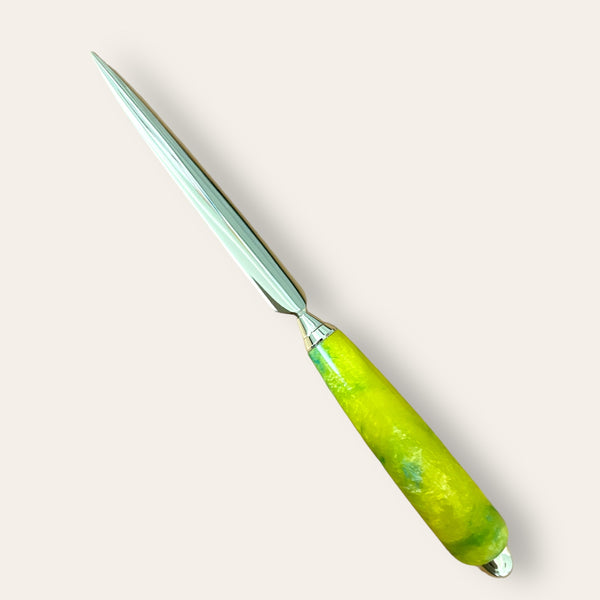 Paul's Hand Turned Creations presents the Resin Hand Turned Letter Opener - Sunbeam, featuring a sharp, pointed blade and a handle with a distinctive hand-turned design in green and yellow marbled material. The smooth, glossy finish of the handle contrasts beautifully against the plain, cream-colored background, making it an elegant gift for any occasion.