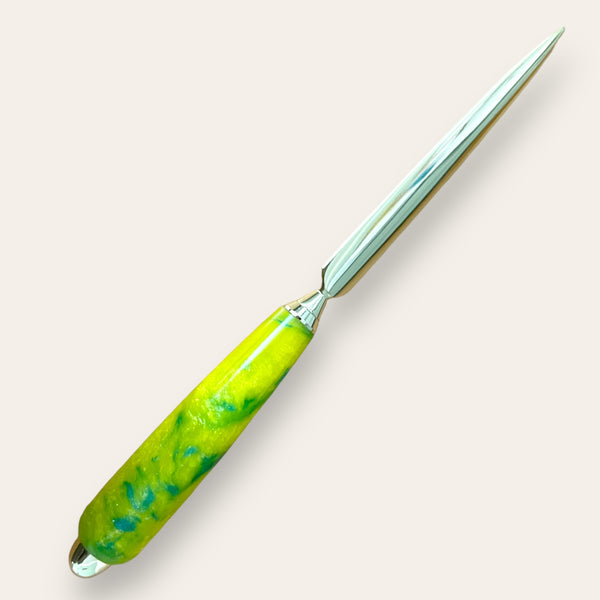 The Resin Hand Turned Letter Opener - Sunbeam by Paul's Hand Turned Creations features a shiny, metal blade and a handle with a hand turned design marbled in yellow and green tones, displayed against a light beige background.