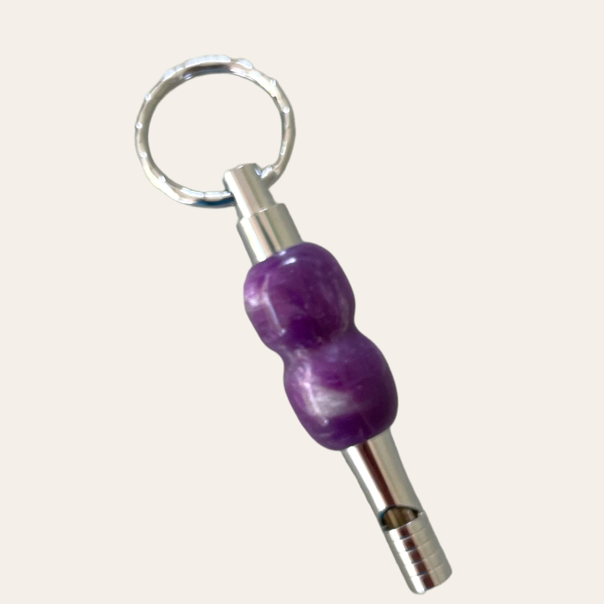 The Lilac Resin Key Chain with Safety Whistle, created by Paul's Hand Turned Creations, is a small, cylindrical whistle featuring a metallic body and a purple, textured grip in the middle. Its silver, textured keyring allows for easy attachment to keychains or other items, ensuring this unique accessory is always within reach.