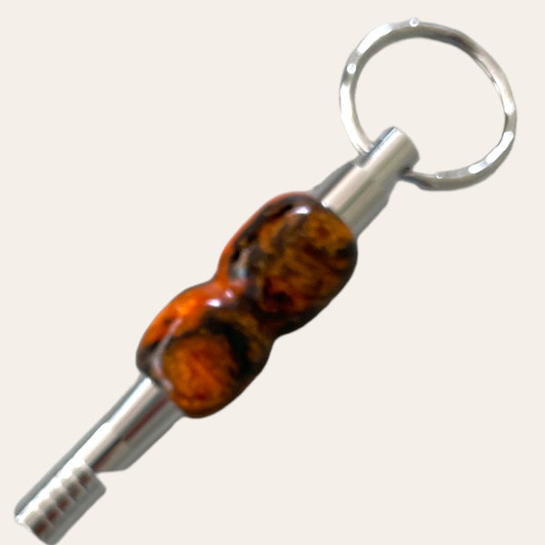 A close-up image of a black and orange resin key chain with a safety whistle from Paul's Hand Turned Creations. The key chain has a slender, cylindrical shape with a textured surface, making it both a practical accessory and a unique gift idea for any enthusiast.