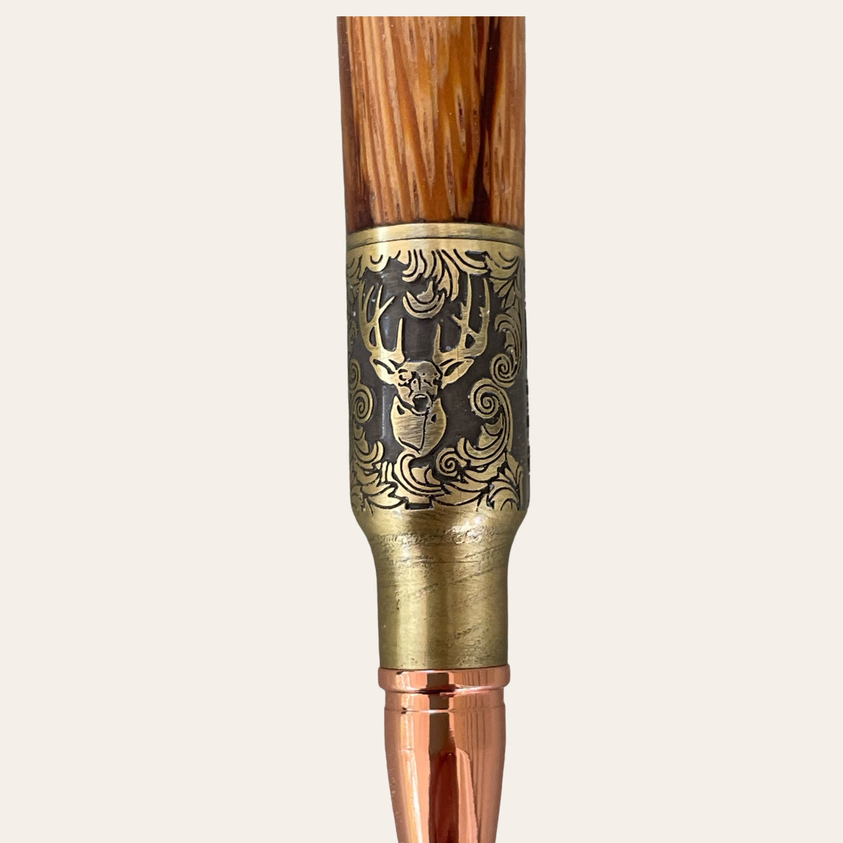 Close-up of the Hand Turned Deer Hunter Bolt Action with Antique Brass - Zebrawood pen by Paul's Hand Turned Creations. The metallic section features an engraved design depicting a detailed image of a stag with antlers surrounded by ornate patterns. This handcrafted pen boasts a golden tip and bolt action mechanism for seamless writing.