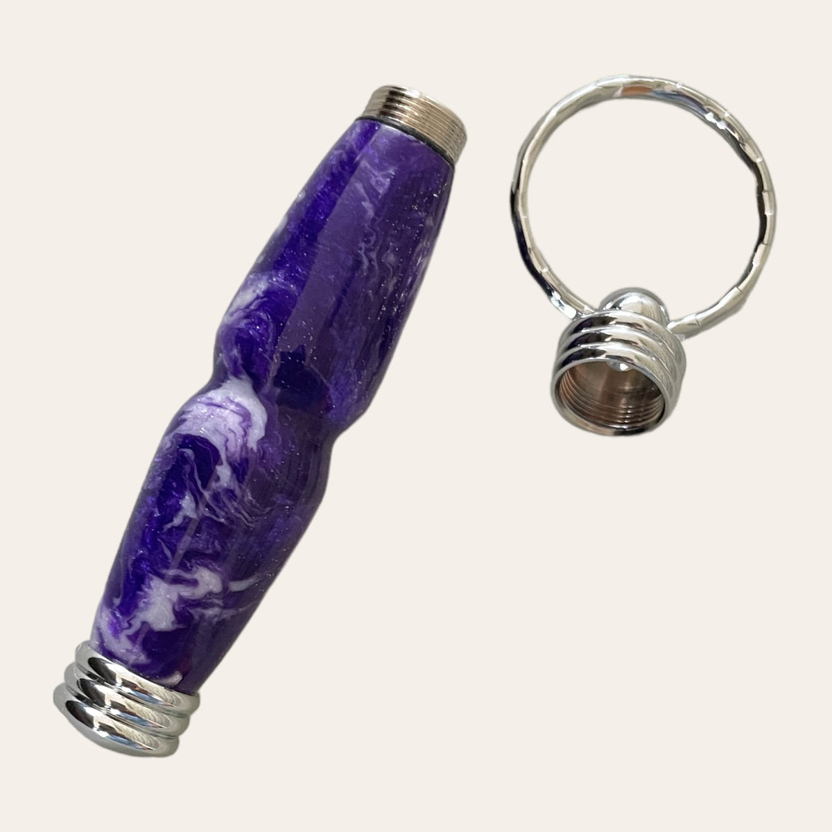 A beautifully crafted, hand-turned resin pen named "Purple Passion" by Paul's Hand Turned Creations, features a purple and white marbled design with a silver ring cap. Displayed separately on a light background, it boasts a curvy, ergonomic shape and ridged metallic detailing on the cap. Ingeniously designed, this detachable pen includes a hidden compartment keychain for added utility and style.