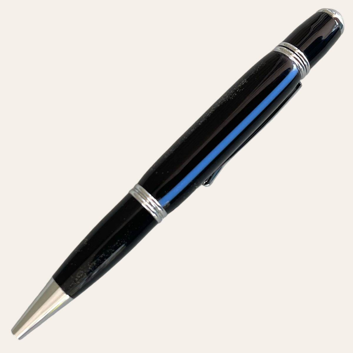 A black ballpoint pen with chrome trim on the clip, tip, and ring, shown on a light background. The glossy finish of this Hand Turned Thin Blue Line Gatsby Pen from Paul's Hand Turned Creations adds a sleek and elegant touch suitable for professional or personal use.