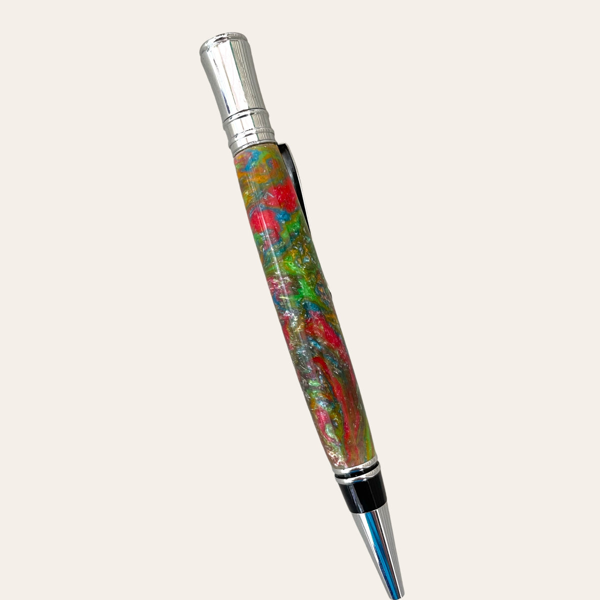 Introducing the Refillable Resin Executive Pen With Chrome Trim - Mysterious by Paul's Hand Turned Creations. This ballpoint pen features a metallic tip and cap, with a body decorated in a colorful, marble-like pattern in shades of green, red, and blue. The sleek black clip is attached near the top for convenience. Handmade for exceptional quality, this executive pen includes a Parker-style refill on an elegant off-white background.