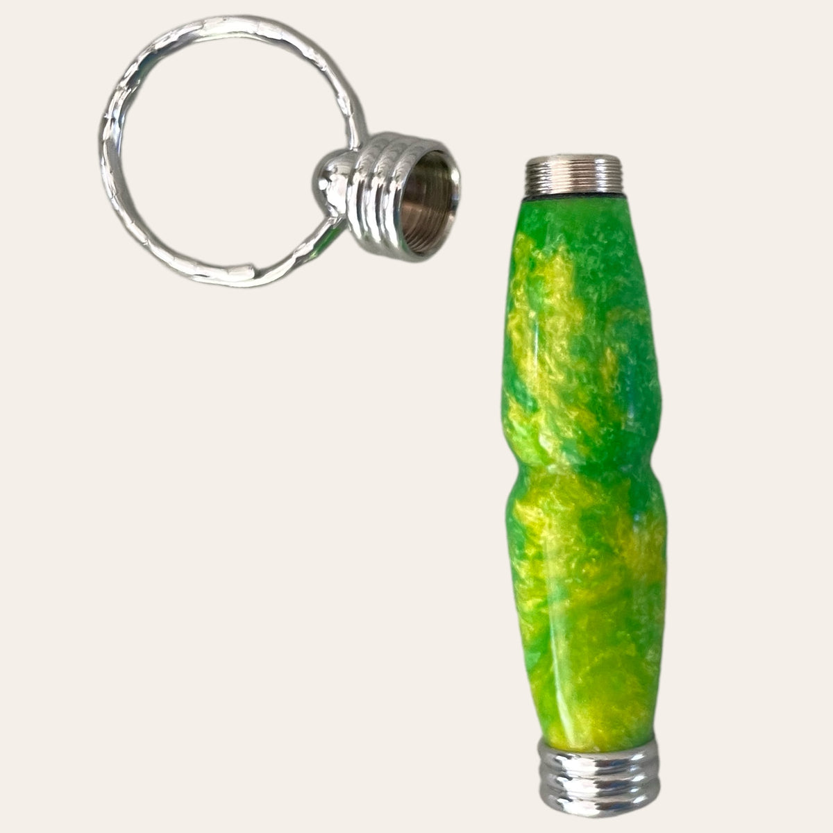 The Hand Turned Resin Secret Compartment Key Chain - Lemon Lime by Paul's Hand Turned Creations is a small, colorful accessory featuring a textured green and yellow cylindrical body made of durable resin with silver-colored metal ends. The cap can be unscrewed to reveal the threaded opening next to the Secret Compartment Key Chain. It includes a silver ring for easy attachment to keys or other items.