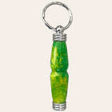 A close-up view of Paul's Hand Turned Creations' Hand Turned Resin Secret Compartment Key Chain - Lemon Lime, showcasing a bright, cylindrical charm. The charm is crafted from durable resin in a primary green color with yellow marbling and features silver metal accents at both ends. The keychain ring itself is metallic and textured. The background is plain and off-white.