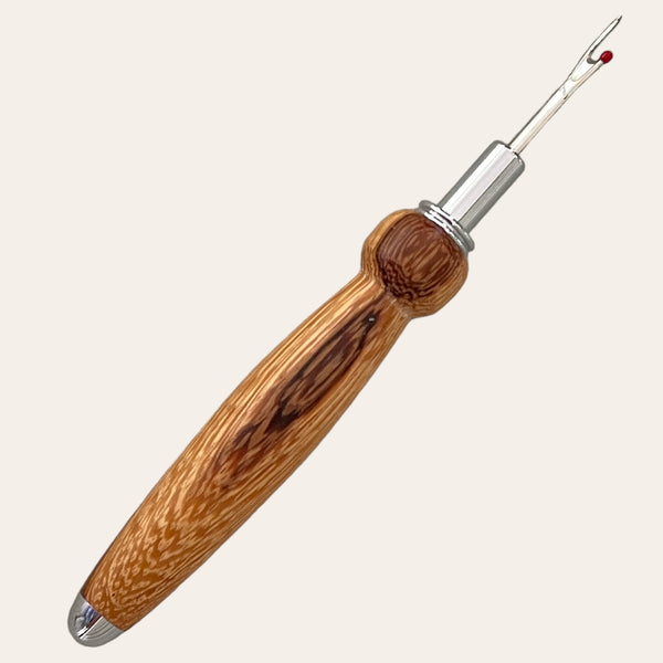 The Zebrawood Hand Turned Single Blade Seam Ripper by Paul's Hand Turned Creations features a polished zebrawood handle with darker grain patterns and a hook-shaped stainless steel blade equipped with a small red ball, making it the perfect tool for removing stitches.