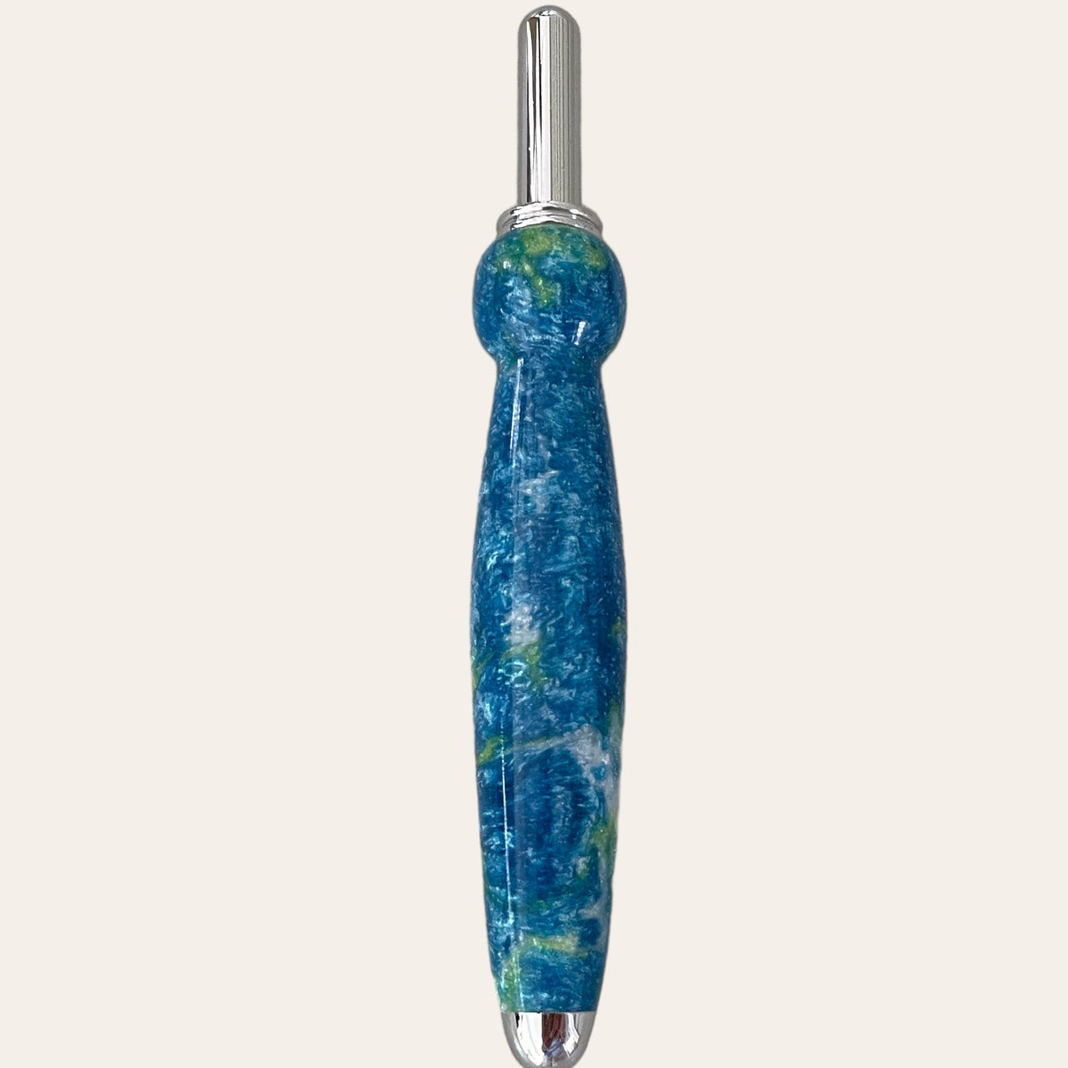 A uniquely designed seam ripper with a blue and green marbled resin handle, featuring a rounded grip and silver metal accents on both ends. This tool, reminiscent of a finely crafted pen, stands vertically against a plain background. The product is known as the "Under The Sea Resin Single Blade Seam Ripper" by Paul's Hand Turned Creations.