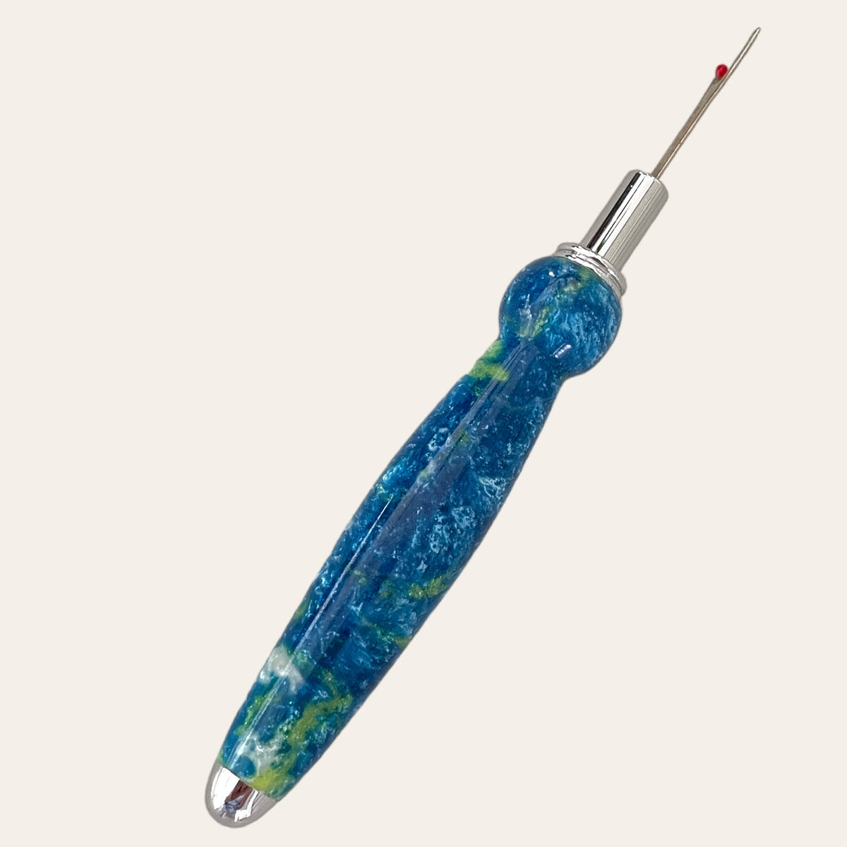 Introducing the "Under The Sea Resin Single Blade Seam Ripper" by Paul's Hand Turned Creations. This handmade seam ripper features a striking blue and green marbled design with a silver-toned removal head, topped with a vibrant red protective cap. Its ergonomically shaped handle ensures a comfortable grip for effortlessly removing stitches in both sewing and crafting projects, making it an essential tool that truly stands out against any plain white background.