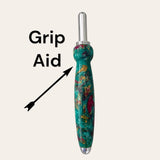 An image of the Royal Jewels Resin Single Blade Seam Ripper, a grip aid tool from Paul's Hand Turned Creations, featuring a shiny metal top and a handle with green, red, and gold swirls. The tool is labeled 