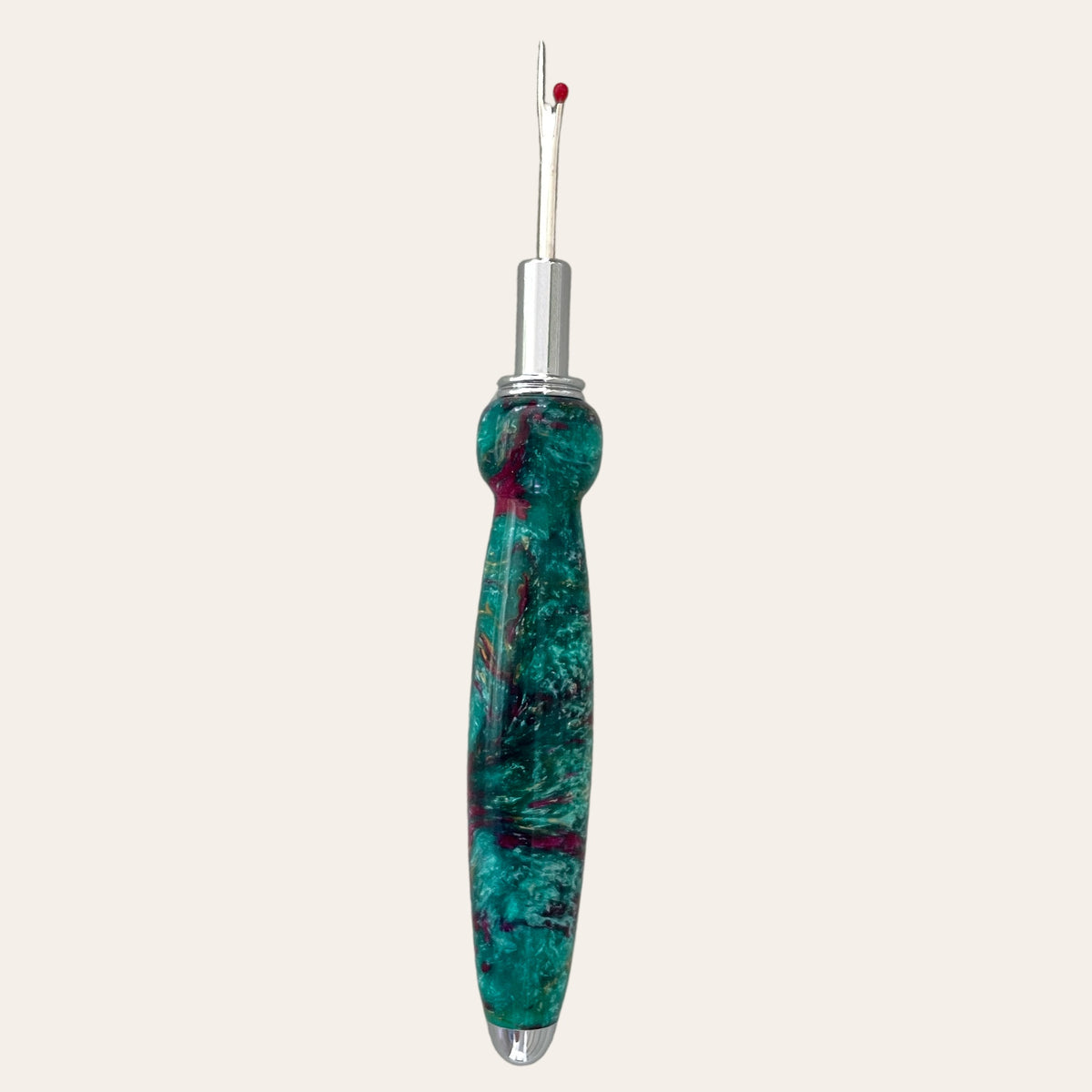 Introducing the Royal Jewels Resin Single Blade Seam Ripper by Paul's Hand Turned Creations. This indispensable sewing tool features a vibrant, marbled handle adorned with shades of green, blue, and red. It comes equipped with a thin, pointed stainless steel blade and a distinctive red ball at the tip, making it perfect for removing stitches in fabric.