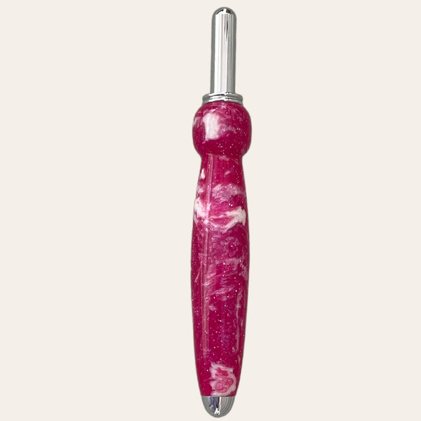 A Magenta Resin Single Blade Seam Ripper from Paul's Hand Turned Creations, featuring a shiny silver blade and a pink marbled handle with a rounded grip for comfortable use, is displayed vertically against a plain white background.