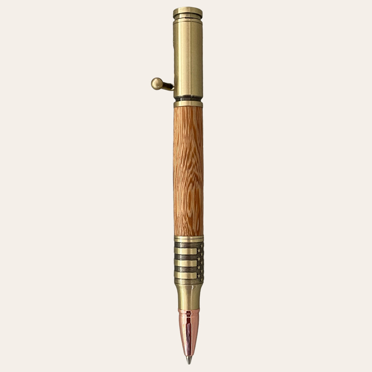 The Zebrawood Salute The Troops Bolt Action Hand Turned Pen by Paul's Hand Turned Creations features an antique brass finish on the metal top and bottom sections, a wooden body made from zebrawood, and a small bolt action lever on the upper metal part. The refillable pen boasts a detailed tip that elegantly combines classic metal with natural wood design elements, set against an off-white background.