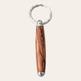 Presenting the Small Bethlehem Olive Wood Keychain by Paul's Hand Turned Creations – a distinctive keychain with a polished wooden handle characterized by rich, natural grain patterns. This exquisitely handcrafted handle is connected to a sleek, shiny silver ring at the top, with silver elements also capping both ends of the handle for an added touch of elegance.