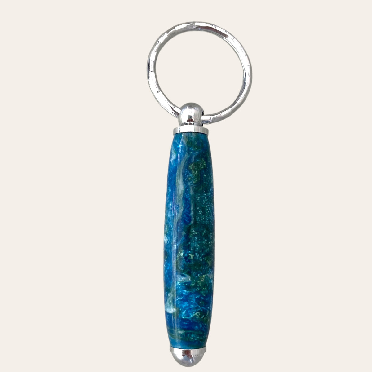 A handcrafted, small resin keychain by Paul's Hand Turned Creations, featuring a cylindrical blue and green marbled pendant with a smooth, polished finish. This unique "Under The Sea" pendant is attached to a metallic ring for holding keys.