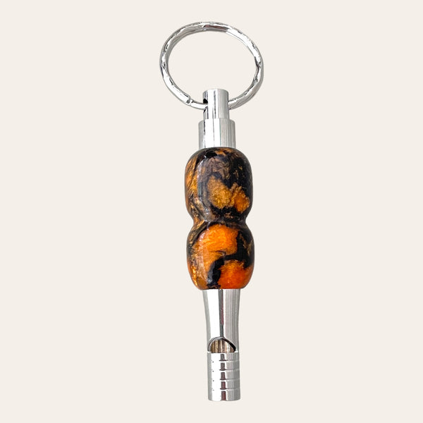 Introducing the Black and Orange Resin Key Chain with Safety Whistle by Paul's Hand Turned Creations. Perfect as a unique gift idea, this small metallic whistle comes with a silver ring attachment and features a distinct handle adorned with swirled patterns in orange, black, and brown hues for a stunning marbled effect. This sleek and polished keychain is not only stylish but also highly practical.