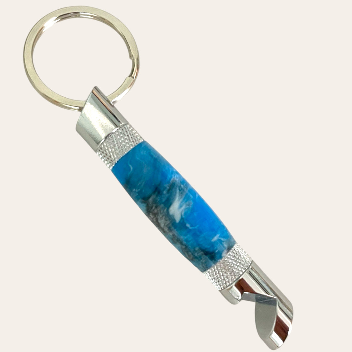 Paul's Hand Turned Creations presents the Chrome Hand Turned Bottle Opener Resin Keychain in Bluebird. This elegant accessory features a sleek silver bottle opener and a durable handle with a blue, marbled design. The keyring is securely attached at one end, while the bottle opener is located at the other. The handle is adorned with silver textured bands near both ends for added sophistication.