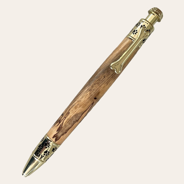 The Spalted Tamarind Dog Click Pen With Gold Trim from Paul's Hand Turned Creations is perfect for any dog lover. This wooden ballpoint pen features a natural grain pattern on the barrel, complemented by gold-colored decorative accents on the clip and tip that showcase intricate cut-out designs. Finished with a slightly glossy sheen and equipped with a retractable mechanism activated by the push-button top, it makes for a personalized accessory.