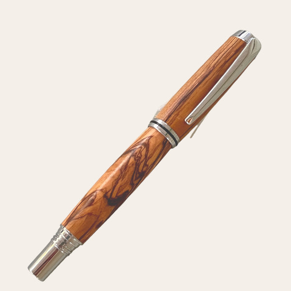 A sleek, handcrafted rollerball pen from Paul's Hand Turned Creations is showcased on a plain background. This polished Hand Turned Exotic Bethlehem Olive Wood Jr. Gentleman Rollerball Refillable Pen boasts silver metallic accents, a stylish design with intricate grain patterns, and a shiny clip on the cap.