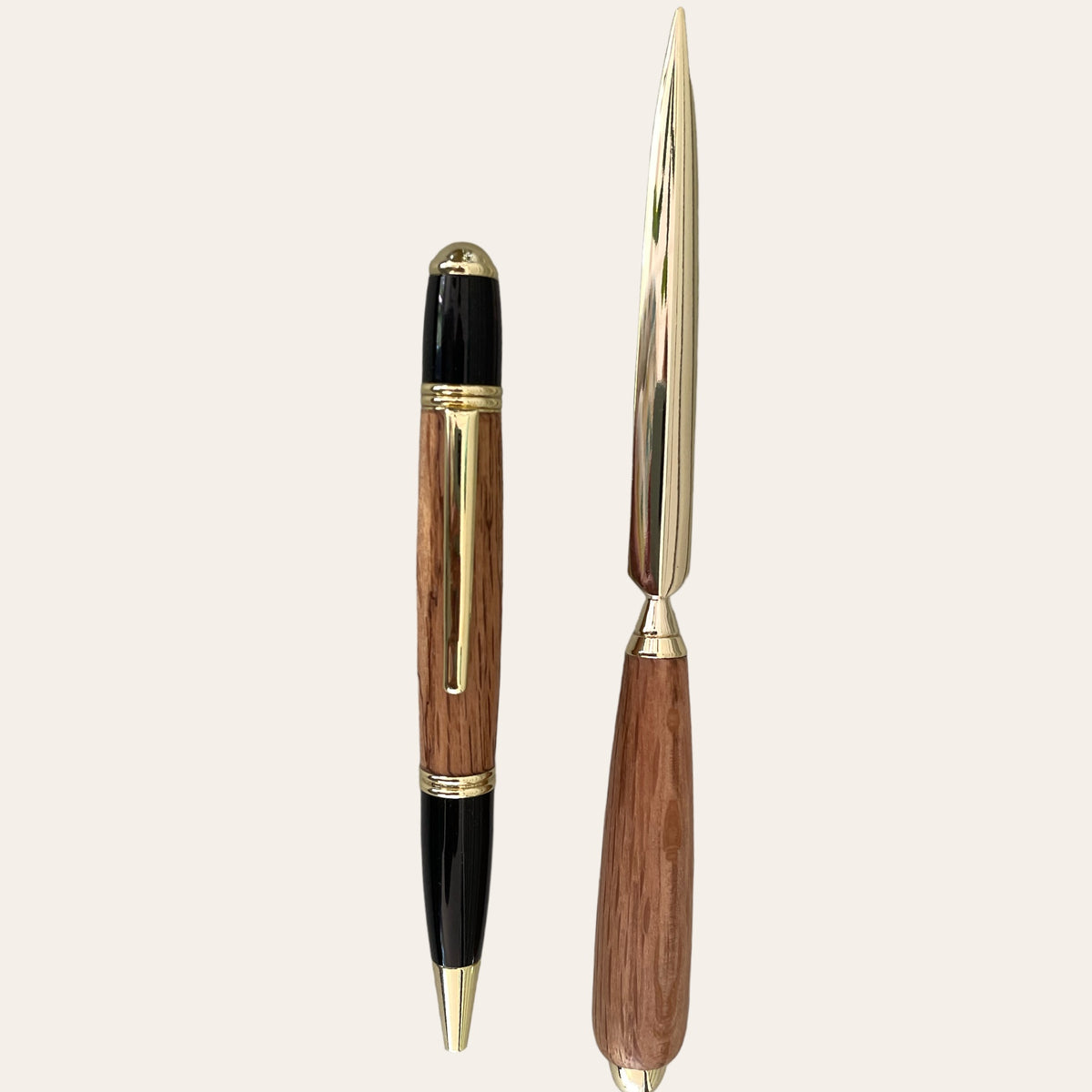 Two elegant writing instruments from Paul's Hand Turned Creations: a closed Handcrafted Gatsby Pen with a black top and bottom, Laurel Oak wood middle, and gold accents; and a gold-tipped letter opener with a wooden handle. Both are displayed vertically against a plain background.