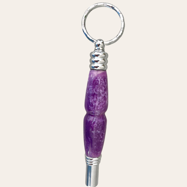 The Lilac Resin Secret Compartment Key Chain with Safety Whistle by Paul's Hand Turned Creations showcases a textured design in purple and silver, complete with a metal ring and a hidden compartment for extra convenience.