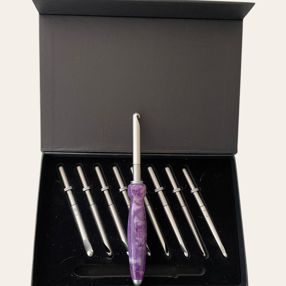 Paul's Hand Turned Creations presents the Hand Turned Resin Crochet Handle with Nine Interchangeable Hooks in a stunning lilac hue, elegantly arranged in an open black box.