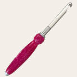 A close-up of the Hand Turned Resin Crochet Handle with Nine Interchangeable Hooks - Magenta by Paul's Hand Turned Creations showcases its sparkly pink handle and silver metal hook. As part of this magenta crochet set, the tool features an ergonomic handle with a bulbous grip designed for comfort during use. The plain light-colored background highlights this essential piece of crochet supplies, making it stand out beautifully.