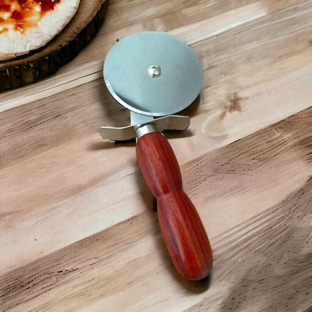 Hand turned wooden handled pizza cutter with stainless steel cutter sitting on a wood table and a small piece of pizza image in the left corner.  Hand turned by Paul's Hand Turned Creations. 