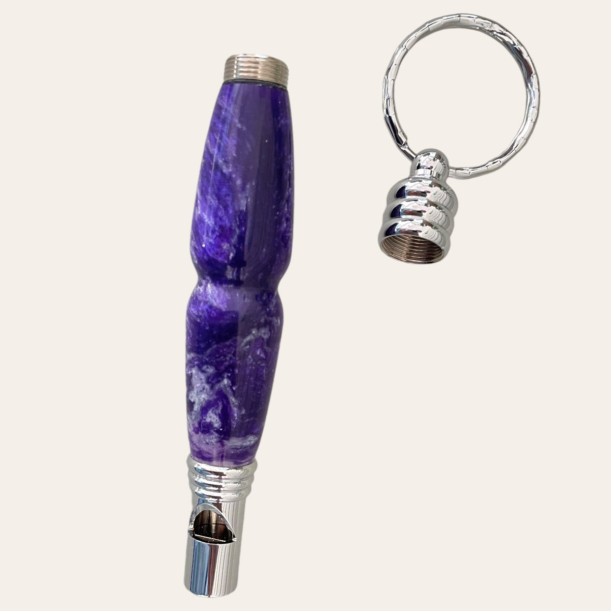 A Purple Passion #1 Secret Compartment Key Chain with Safety Whistle by Paul's Hand Turned Creations, featuring a purple and white marbled metallic whistle with a removable cap attached to a keyring. The whistle boasts a smooth, ergonomic design with shiny metallic ends. When the cap is off and placed next to the whistle, it reveals the keyring attachment and subtly hints at its clever function as a secret compartment keychain.