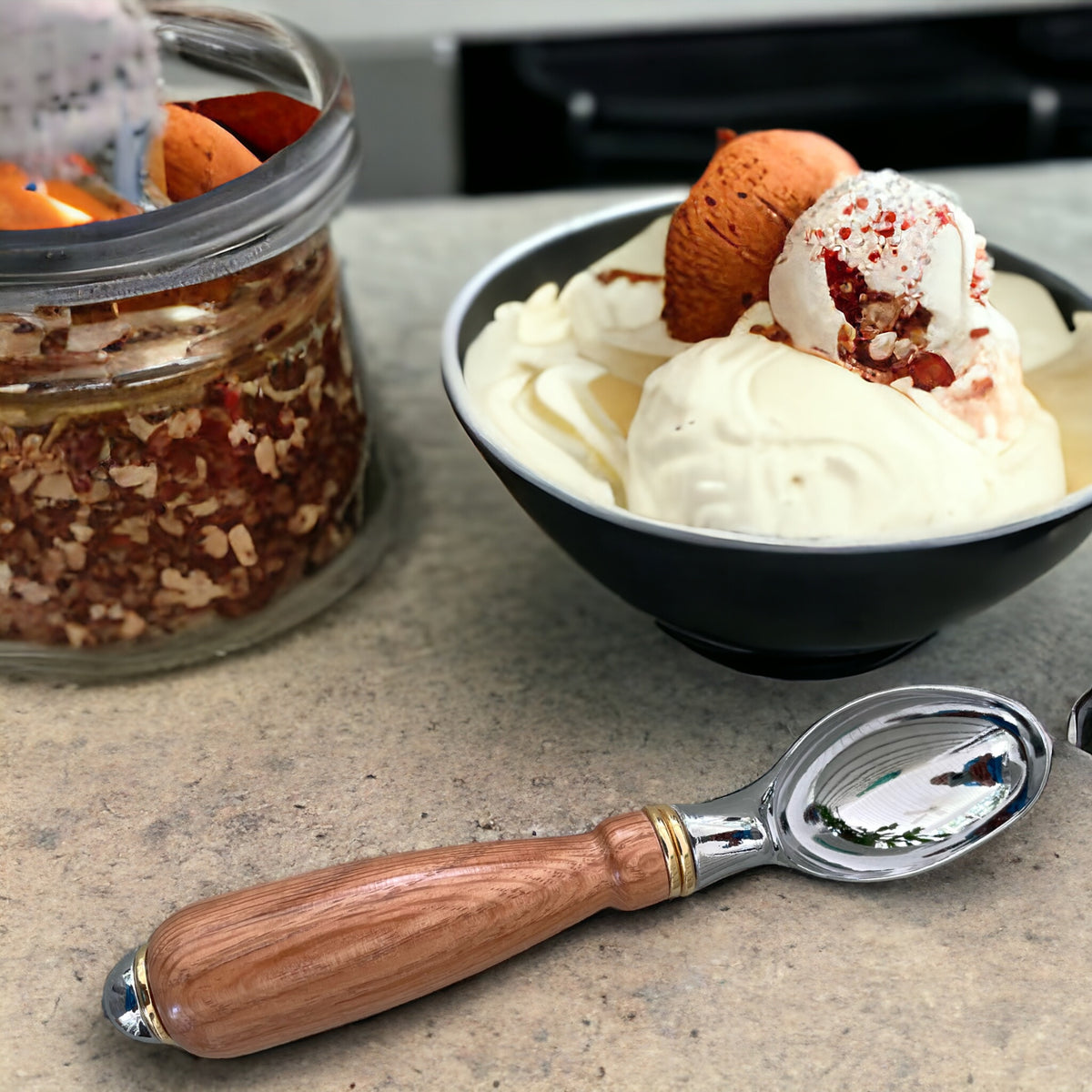 A bowl of vanilla ice cream topped with caramel scoops, nuts, and red sprinkles sits on a countertop next to a glass jar of granola. In the foreground, resting on the counter, is a Red Oak Wood Hand Turned Ice Cream Scoop from Paul's Hand Turned Creations, showcasing unique craftsmanship.