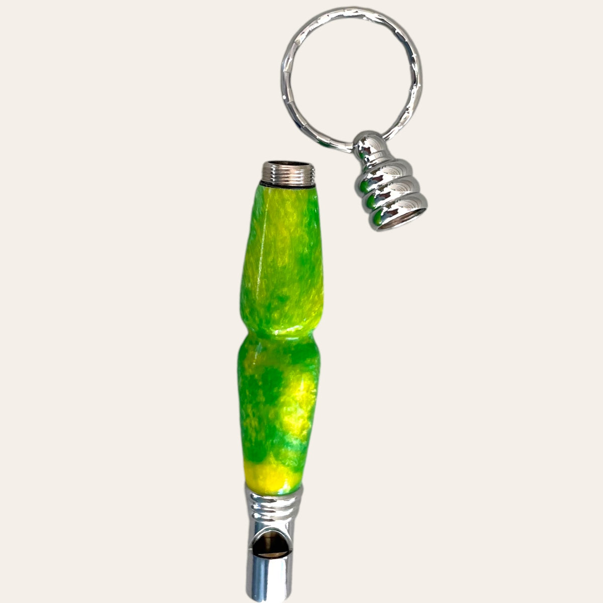 This handmade keychain boasts a cylindrical handle adorned with a smooth, bright green swirl design accented with hints of yellow. The glossy-finished handle seamlessly attaches to a silver keyring at one end, while the other end features a metallic tip. For added functionality, this stylish keychain doubles as a safety whistle. The top does unscrew to place small items inside. 