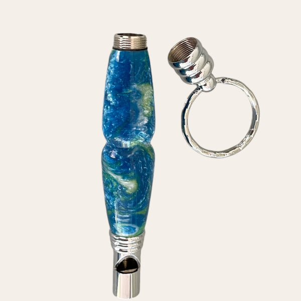 
Hand-turned secret compartment whistle made from resin with blue, white,  and green swirls. The top unscrews to reveal a small storage space inside the barrel.