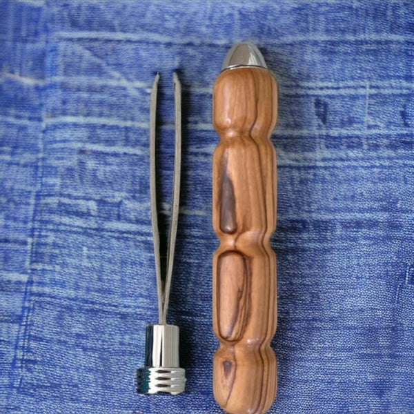 Hand turned stainless steel tweezer next to a bethlehem olive wood case on a blue piece of denim fabric.  Made by Paul's Hand Turned Creations. 